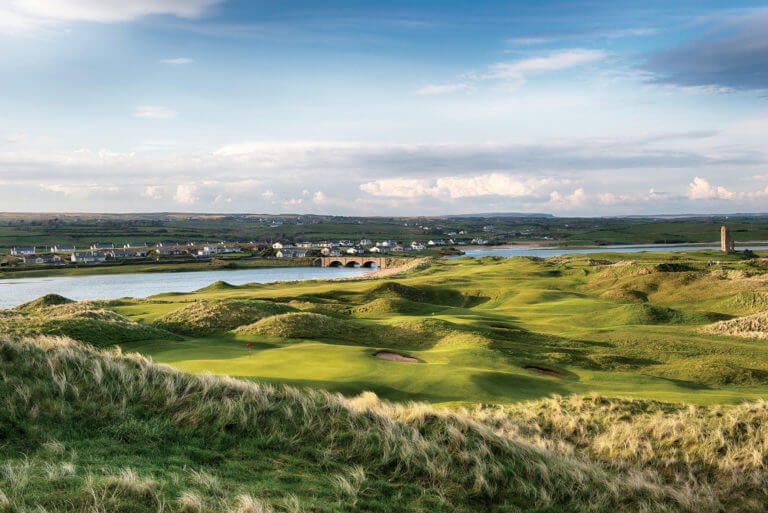 Tenth green stands between towering sand dunes with town in background