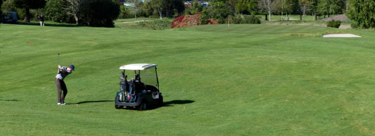 Golfer stands next to a golf cart at Taupo Golf Club