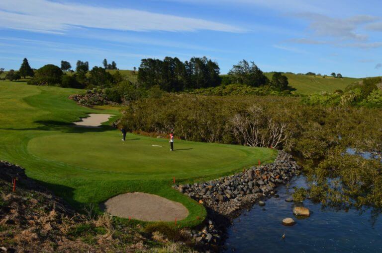 Golfers putt on a green next to the sea
