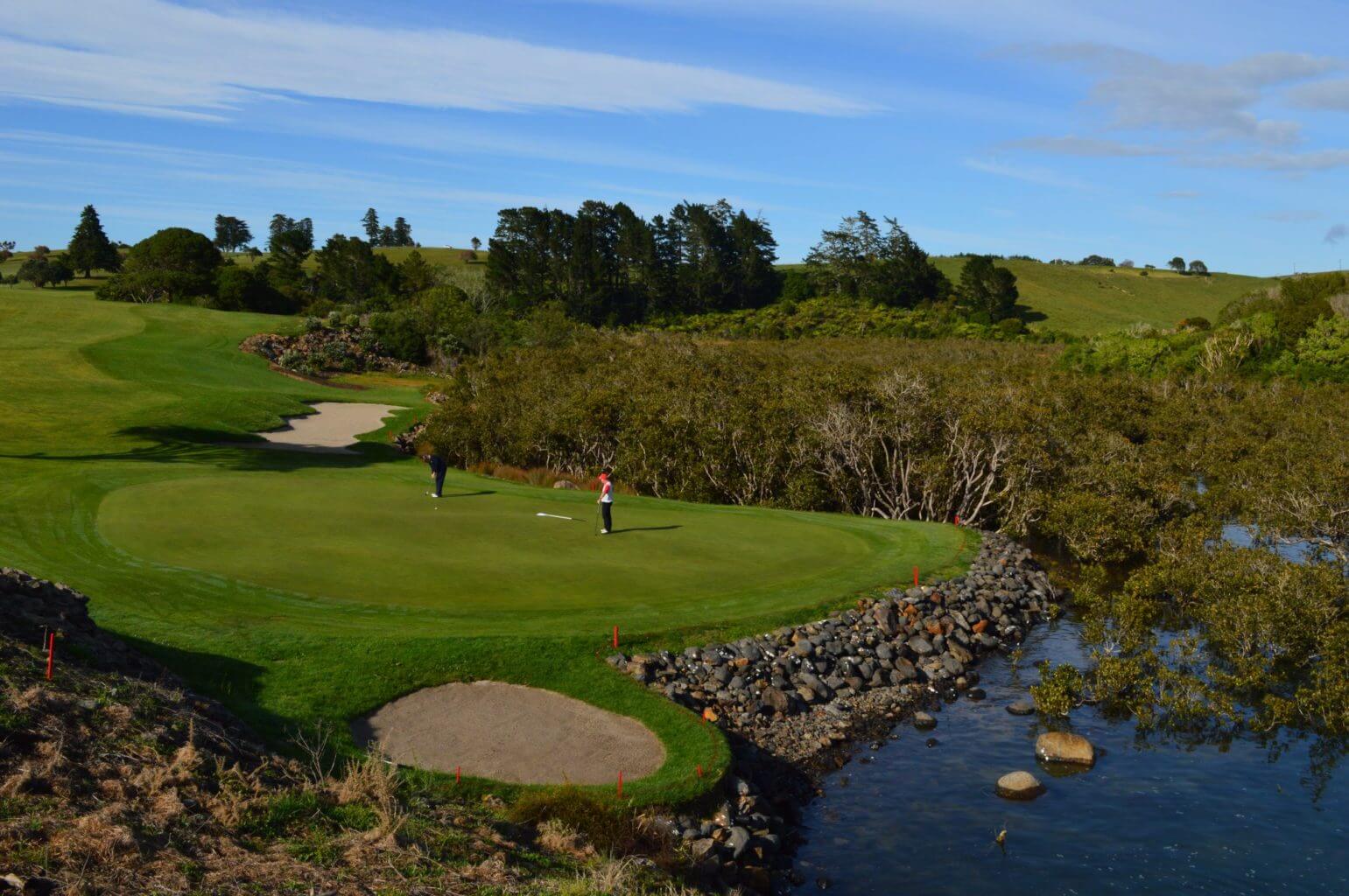 Golfers putt on a green next to the sea