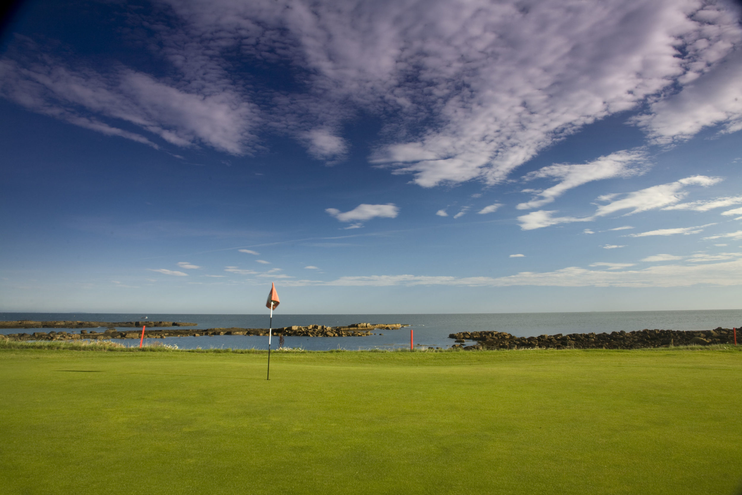 View of a green and rocks fading into the sea from Dunbar Golf Club, Scotland, United Kingdom