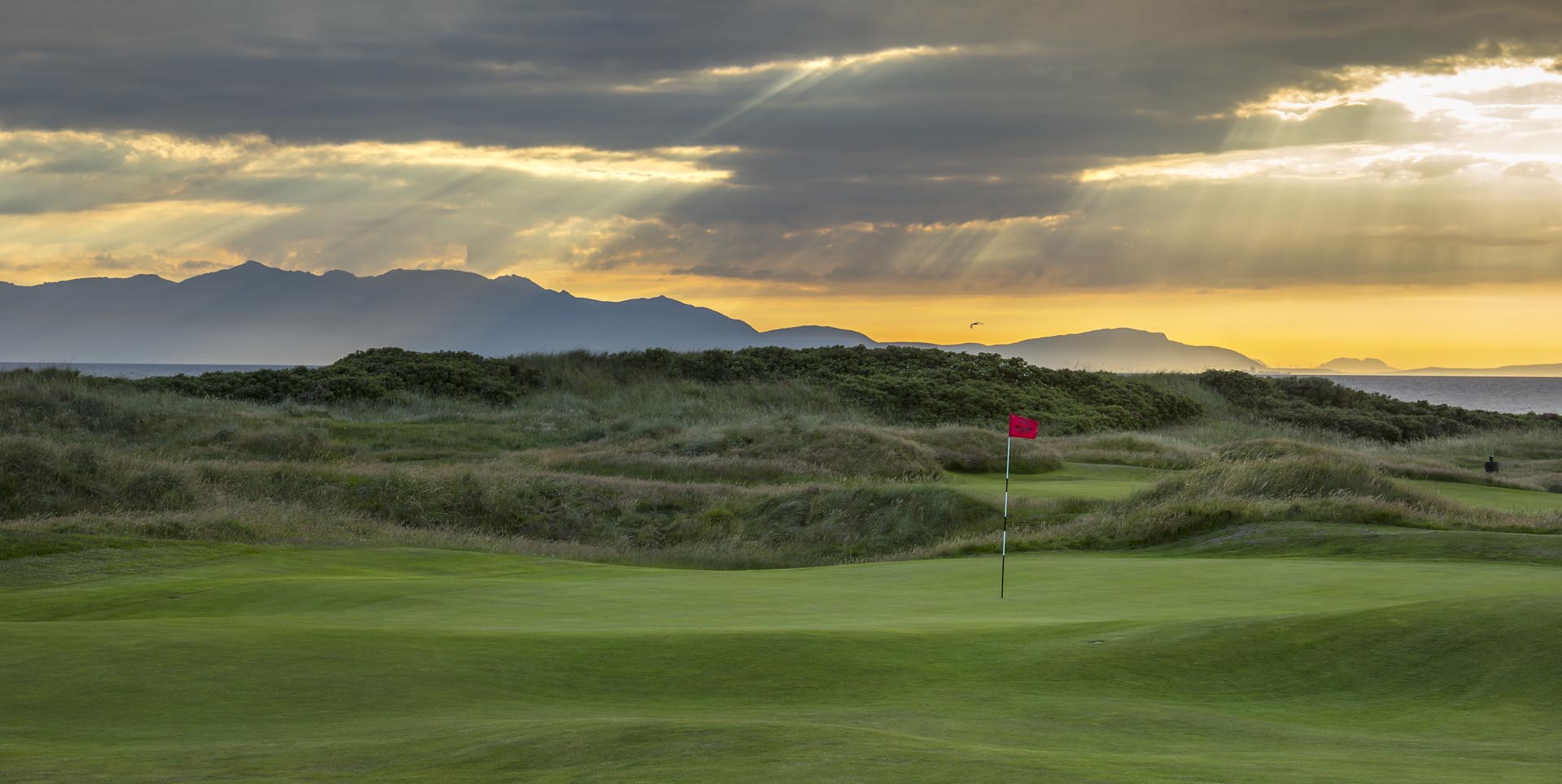 Overlooking a green, sea, and hills on the horizon at The Western Gailes Golf Club, Ayrshire, Scotland, United Kingdom