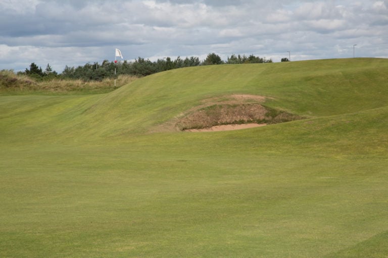 A high rise green shelters the flag from a pot bunker bewlo on the 4th at Gailes Links, Ayrshire, Scotland, United Kingdom