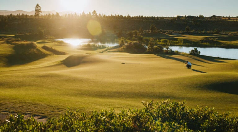 Image of the setting sun casting light on a green and flag on the golf course, Tetherow Resort, Bend, Oregon, USA