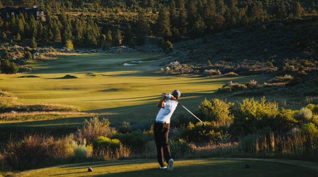 Image of a golf player teeing off on the golf course t Tetherow Resort, Bend, Oregon, USA