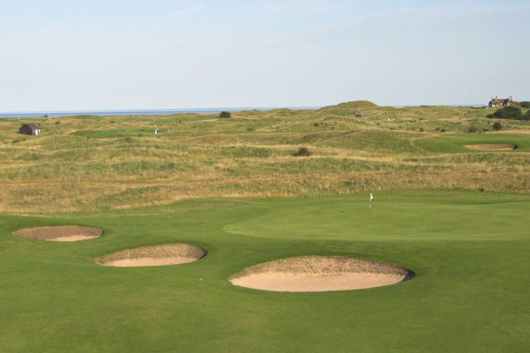 Image overlooking pot bunkers next to a low green with rolling, undulating terrain at Royal St. George's Golf Course, Kent, England