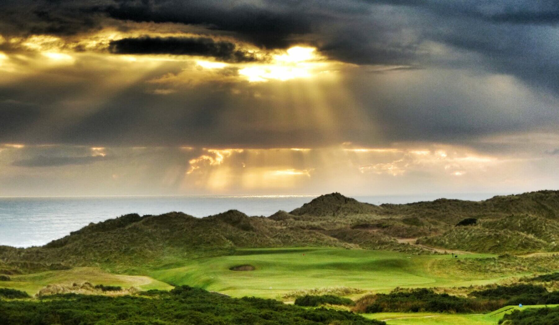 Image displaying shafts of sunlight piercing the clouds over the Cruden Bay Golf Course in Aberdeenshire, Scotland