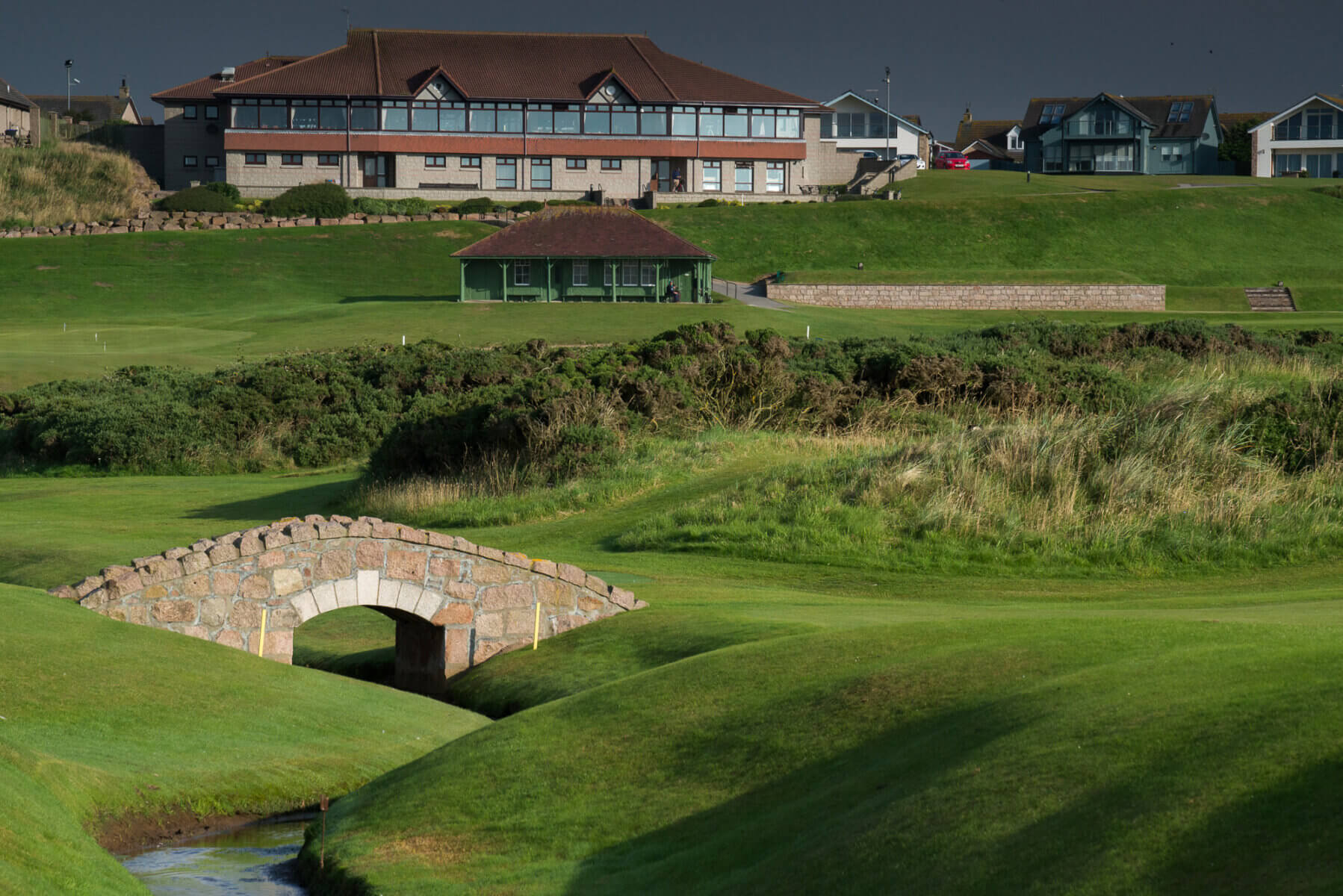 Image displaying a bridge over the 6th fairway and the clubhouse in the background at Cruden Bay Golf club, Scotland