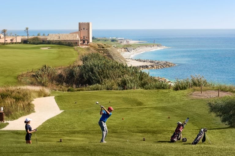 Image of a golfer teeing off with the golf clubhouse in the background, Verdura Resort, Sicily, Italy