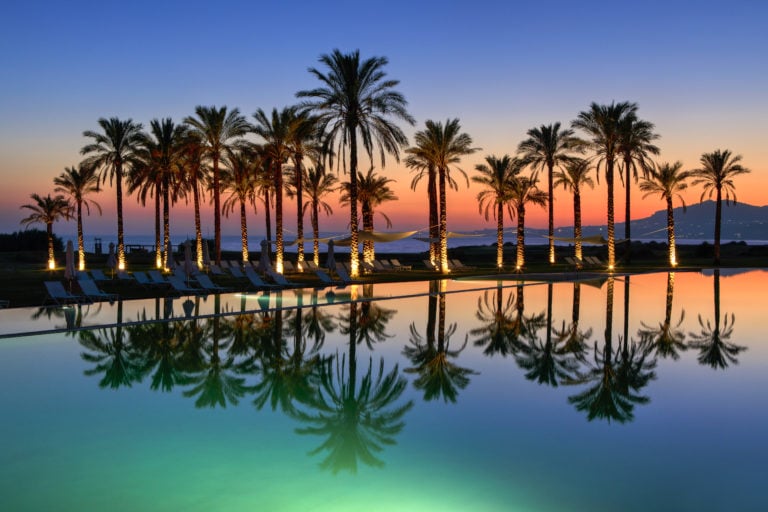 Dusk image of palm tree silhouettes behind the infinity pool at Verdura Resort, Sicily, Italy