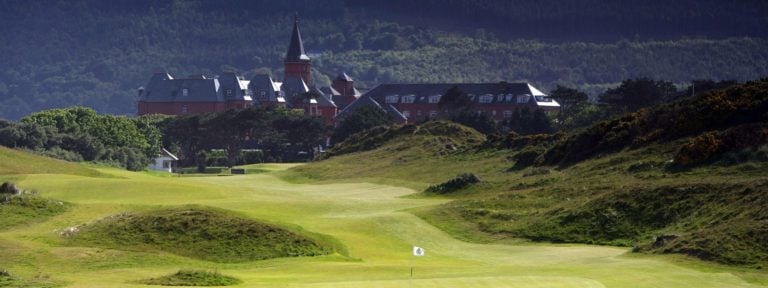 Image depicting the Golf Course and distant spire of the Slieve Donard Hotel behind Royal County Down Golf Club, Northern Ireland