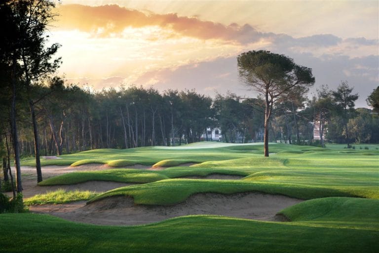 Image displaying the sun setting over undulating bunkers and a lone tree at Montgomerie Links Vietnam Golf Course, Da Nang, Vietnam, Asia