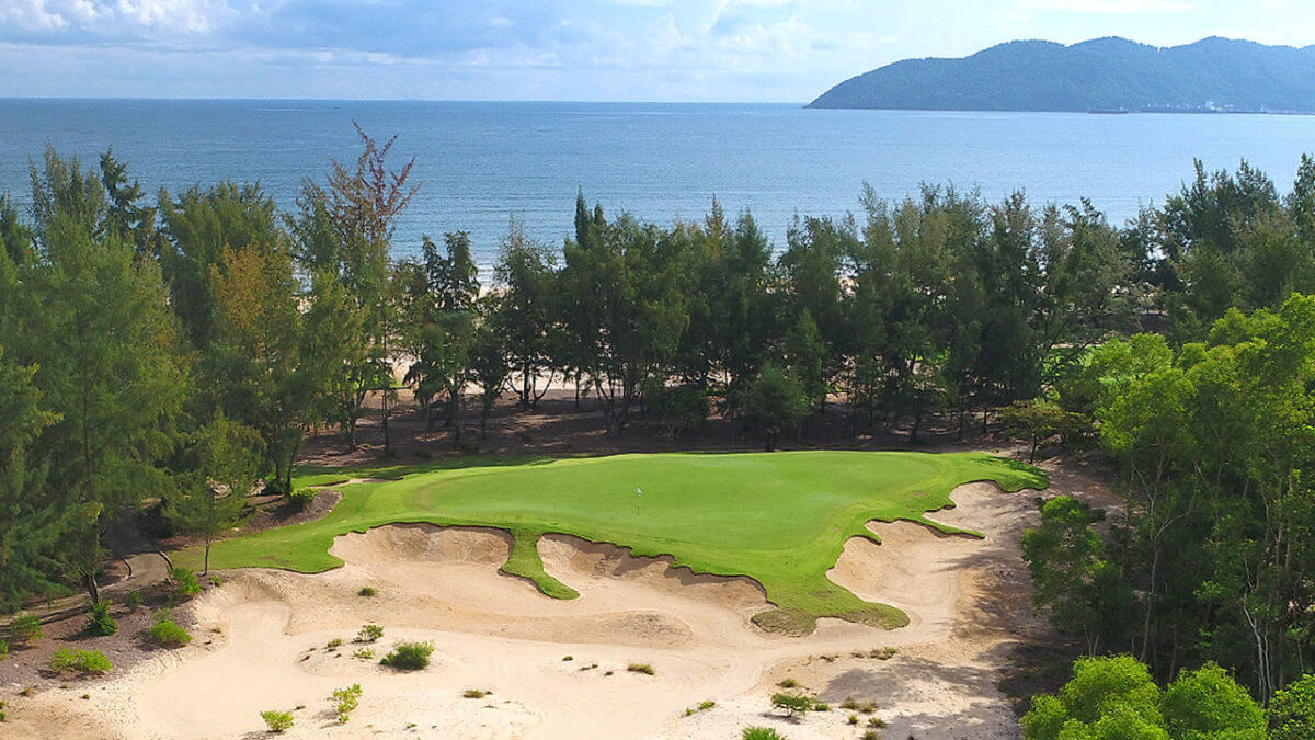 Image of the 6th green with a line of trees separating the golf course from the beach at Laguna Lang Co Golf Club, Da Nang, Vietnam