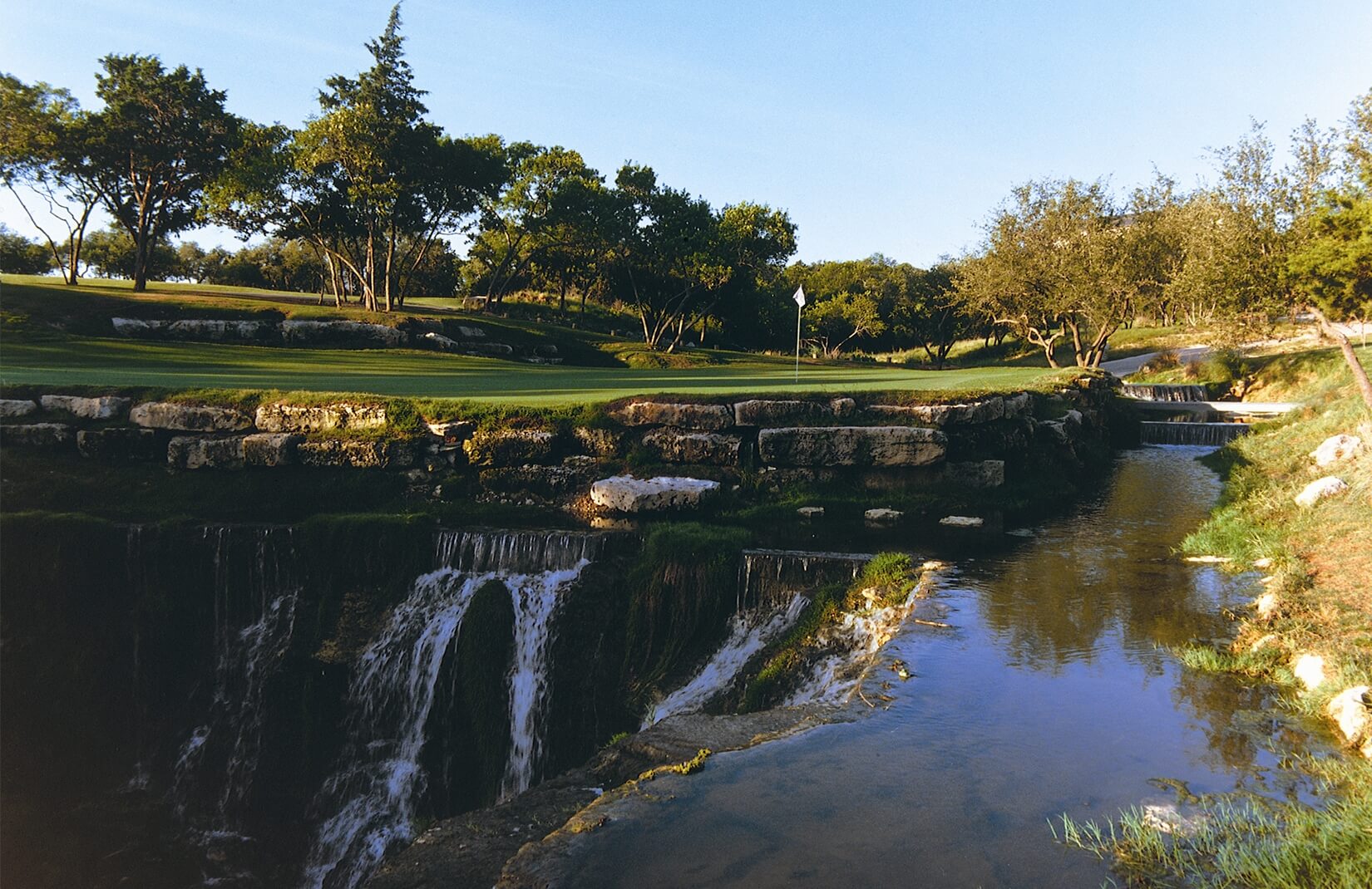 A stone wall separates a green with waterfall