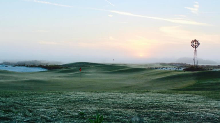 Dawn shows dew on the Black Golf Course with large windmill in the background at Streamsong Golf Resort Black Golf Course