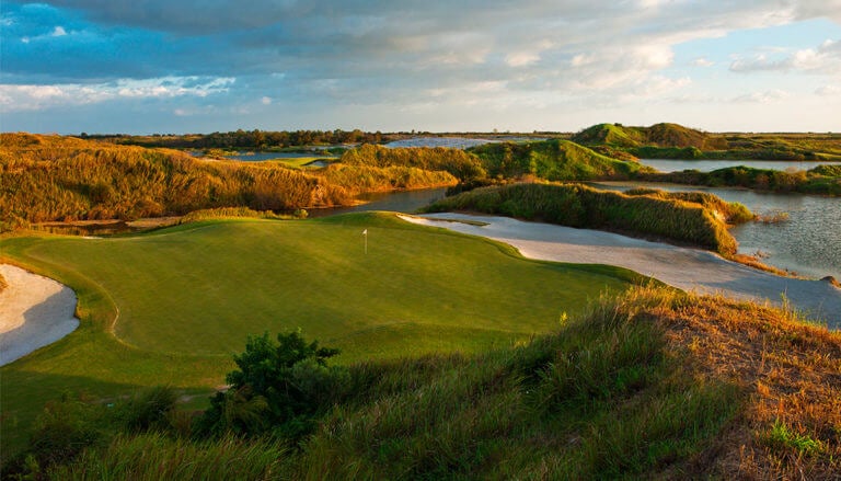 A large green straddled by sand bunkers at dusk on the Red golf Course at Streamsong