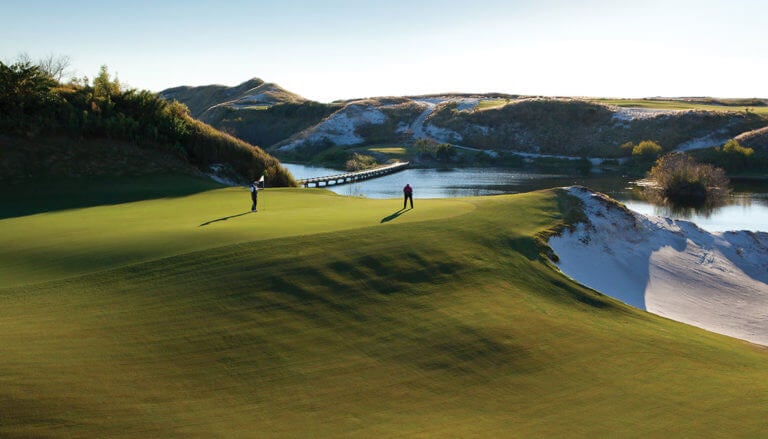 Two golfers putt on the sixteenth green overlooking a lake at Streamsong Golf Resort