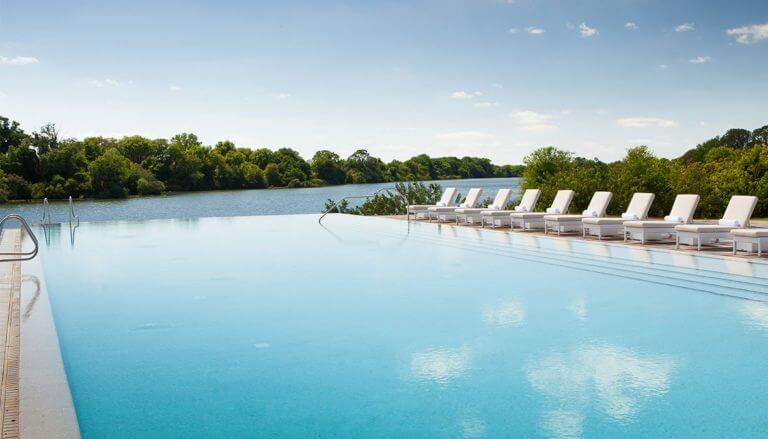 An infinity pool with white lounge recliners overlook a lake at Streamsong Golf Resort in Florida