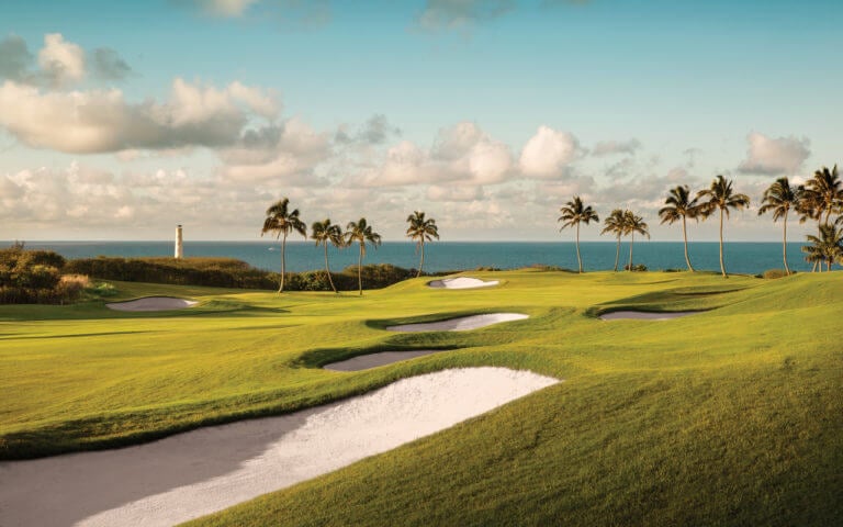 Large sand bunkers lead to a distant golf green with panoramic sea views in Kauai