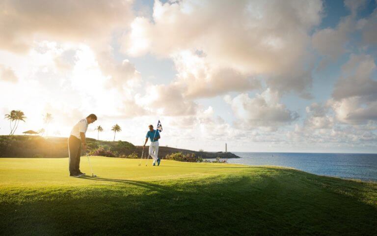 Two golfers play on the putting green at dusk on the Ocean Course at Hokuala in Hawaii
