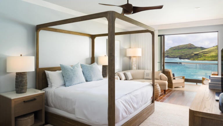 A four-poster bed with contemporary furniture and a balcony overlooks the Pacific Ocean at Timbers Resort in Hawaii