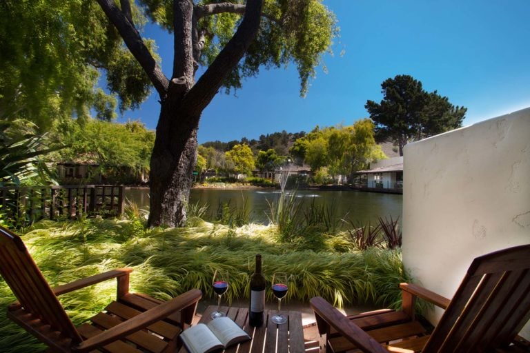 Two reclining chairs with a book and bottle of wine overlook a lake at Quail Lodge Golf Resort in California