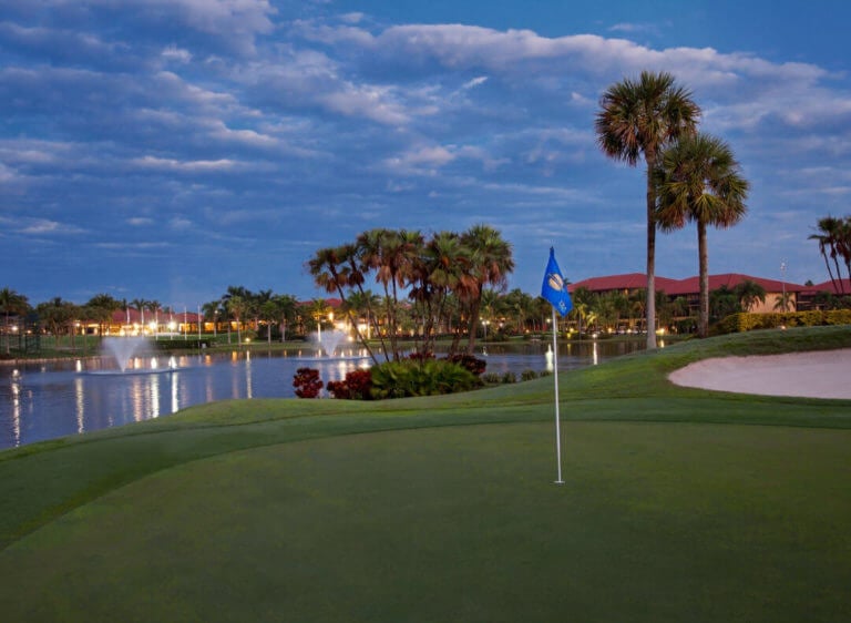 Dawn view of a golf green and distant resort complex over a lake at PGA National Golf Club