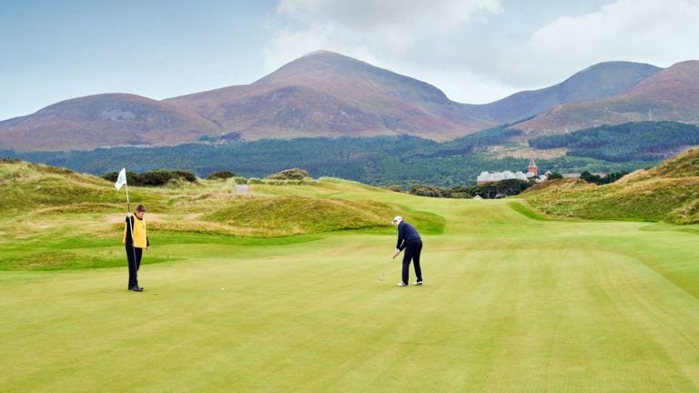 Two golfers on the putting green at Royal County Down Golf Club with Slieve Donard as a backdrop