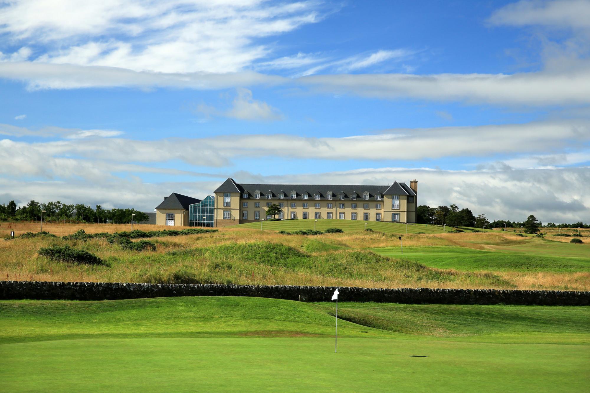 A white flag on a putting green with views of a dry-stone wall and resort building exterior at the The Fairmont Hotel, St Andrews