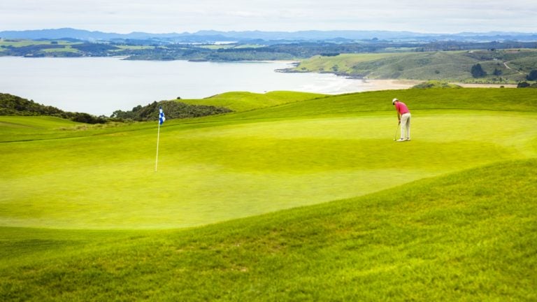 View of a golfer on a putting green overlooking Matauri Bay, New Zealand's North Island