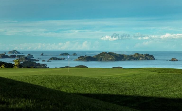 Landscape image of a green at Kauri Cliff's Golf Course and distant Bay of Islands in New Zealand's North Island