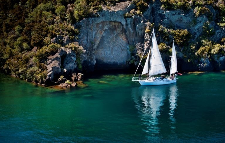 Drone image of Maori rock carvings behind a sail boat on Lake Taupo