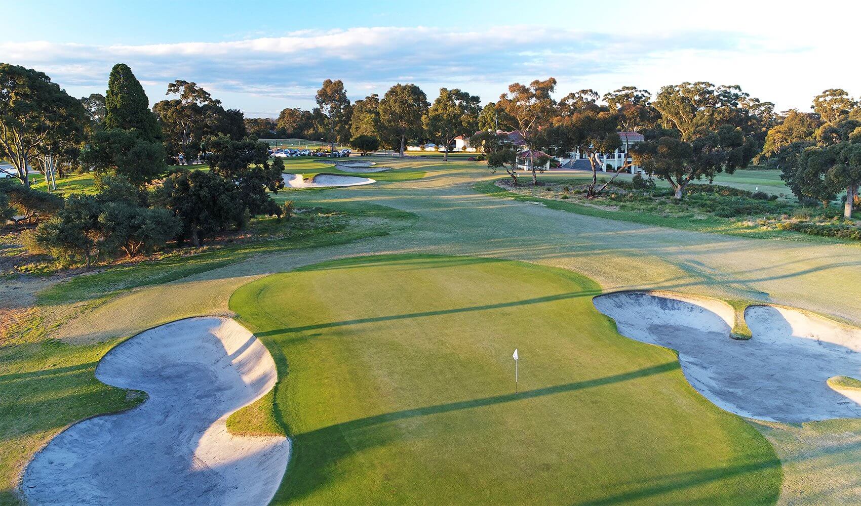 Large sand-bunkers surround a golf green bathed in golden sunlight at Commonwealth Golf Club, Melbourne