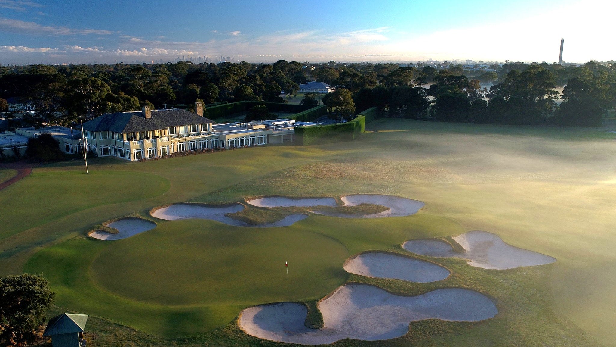 The distant city is seen from above with Royal Melbourne golf clubhouse in the foreground