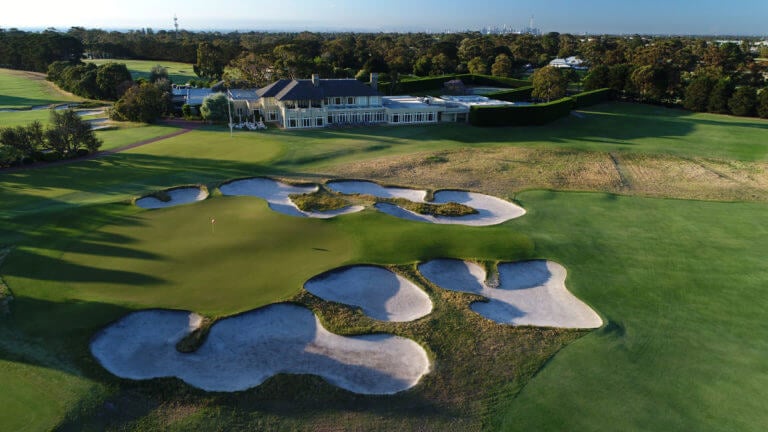 The Royal Melbourne clubhouse overlooks a large green and bunkers on the eighteenth hole