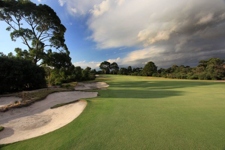 A well-manicured fairway is straddled by sandy bunkers showcasing the Sandbelt golf region