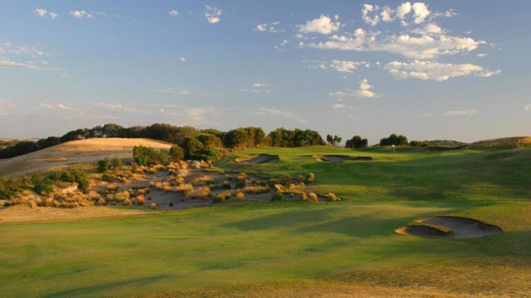 Sunset light shines over a wide fairway leading to raised green