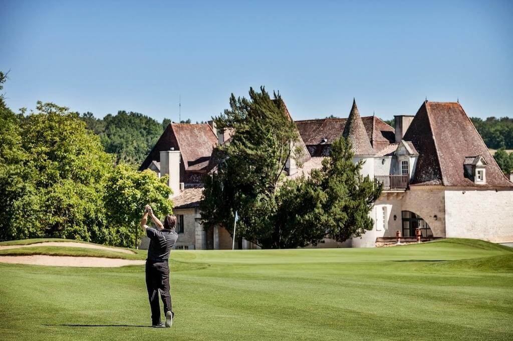 Golfer swings in front of the Chateaux de Vigiers building