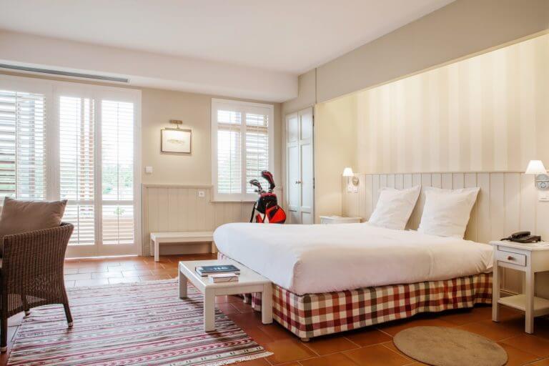 A large king bed lies within a spacious bedroom with space for golf clubs