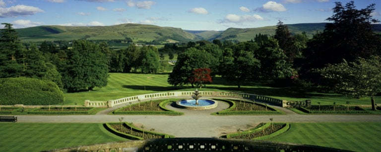 Landscape view of a fountain and manicured garden in front of Scottish Highlands
