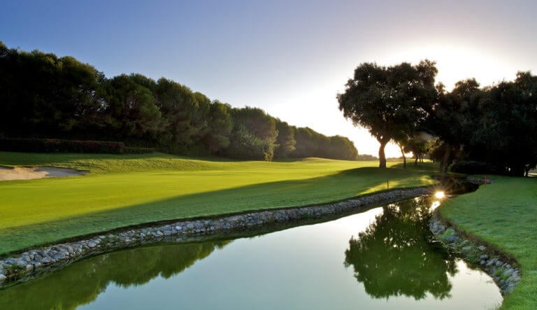 The rising sun casts golden light over the golf course adjacent to a stone-lined canal