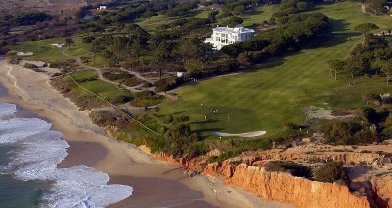 Aerial view of golfers on a green near the beach with distinctive red clay cliffs