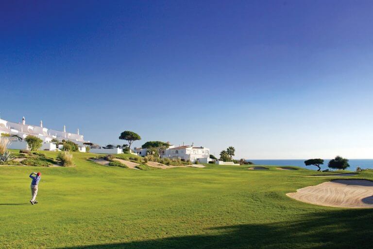 A golfer plays a shot on the Vale do Lobo Royal Golf course with residential houses in the background