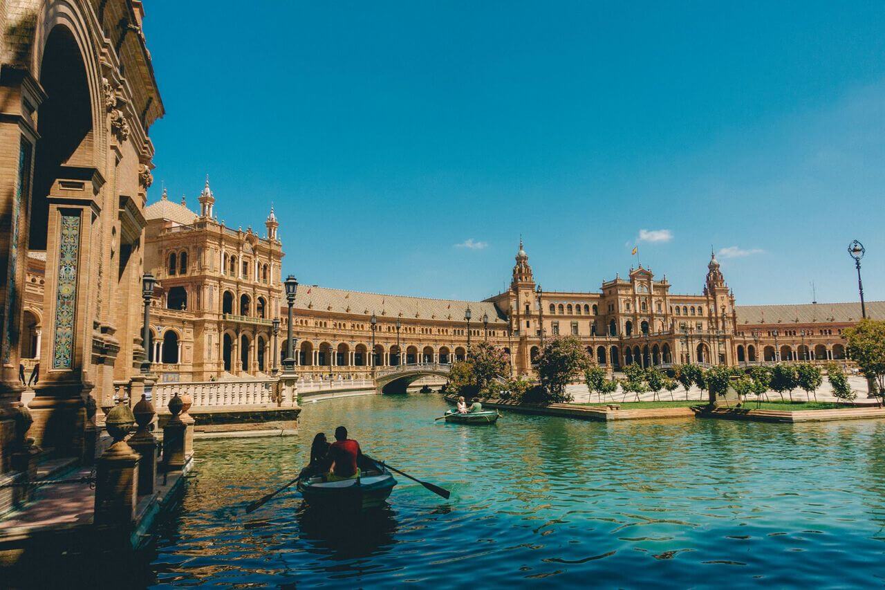 Two people row a boat in Seville's Grand Plaza moat