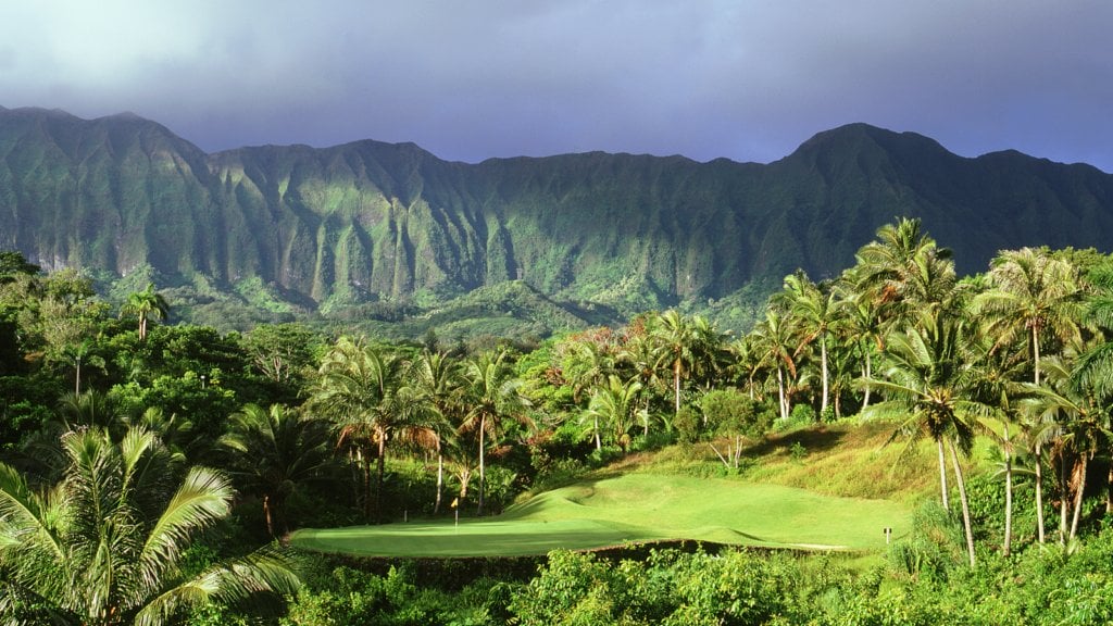 An island green is dwarfed by Hawaiian mountains and vegetation