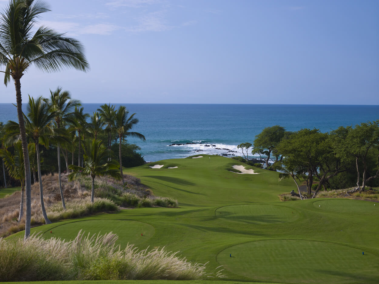 View downhill from a tee to a circular green and Pacific Ocean