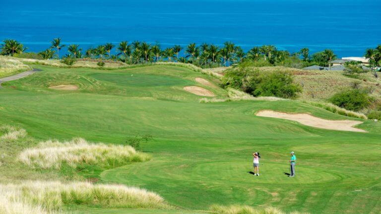 Two golfers stand on a tee overlooking the Pacific Ocean