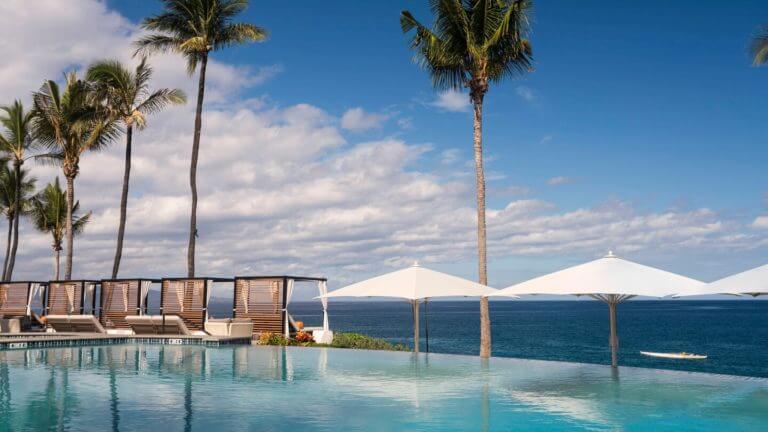 An infinity pool overlooks the Pacific Ocean with cabanas