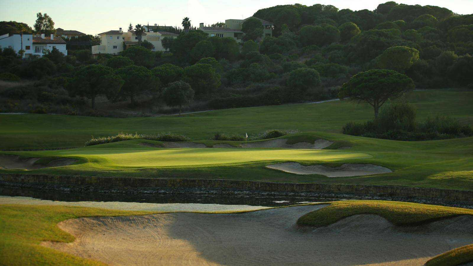 A raised green lies next to large lake in a valley