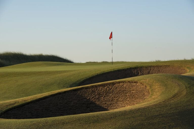 Large pot bunkers lie beneath a red golf flag at The Island Golf Club second hole